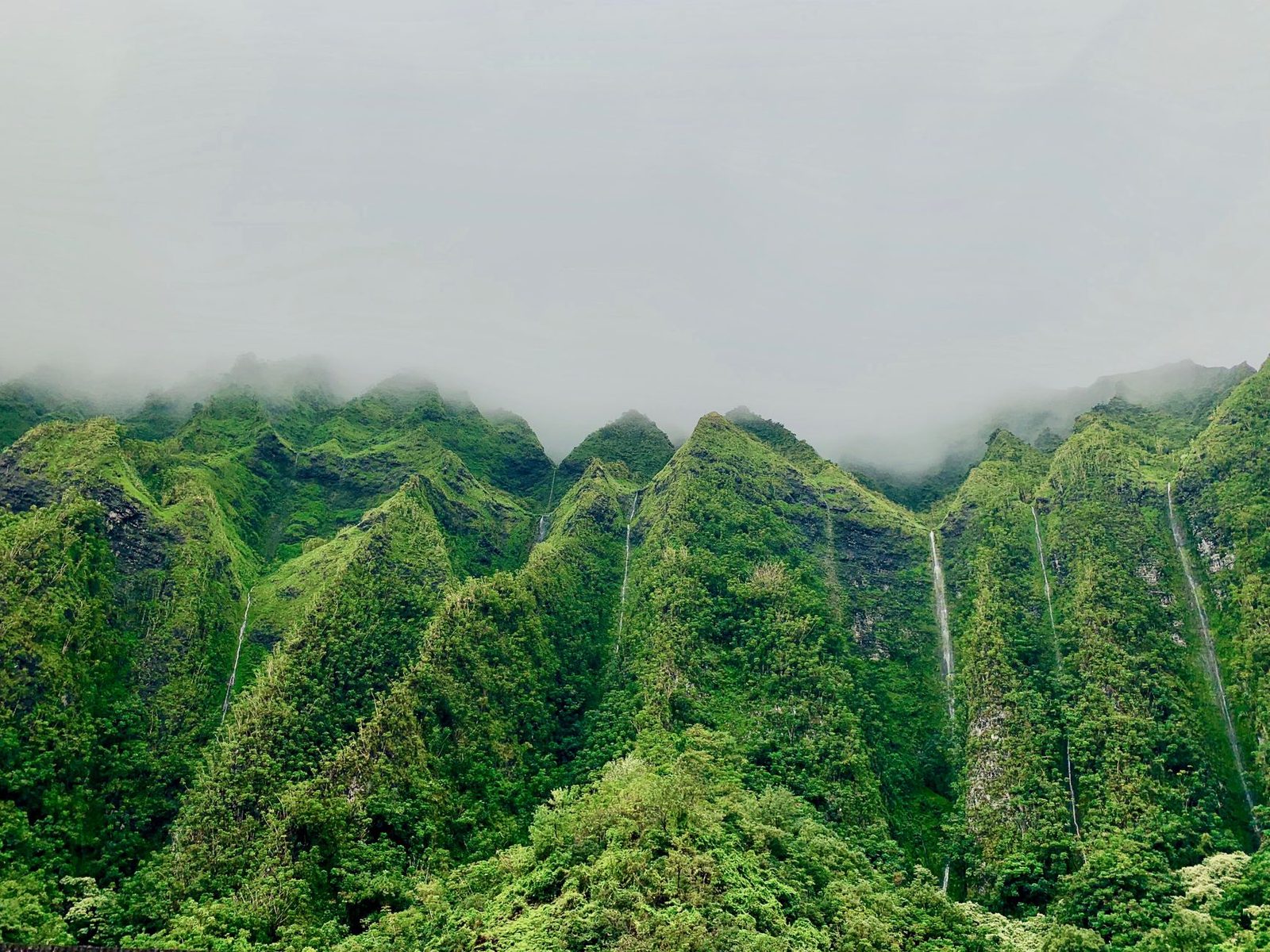Cloud sitting on a steep green ridge with waterfalls running down it, windward Oʻahu